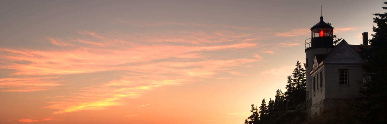 A lighthouse on a rocky coastline overlooking the ocean as the sun sets